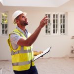 A man wearing a hardhat inspects a newly constructed home.