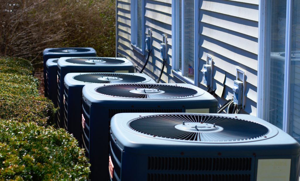 A row of heating and air conditioning units behind a multi-family dwelling.