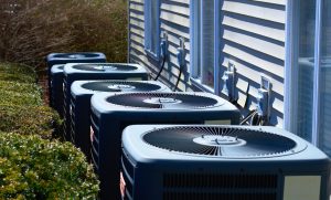 A row of heating and air conditioning units behind a multi-family dwelling.